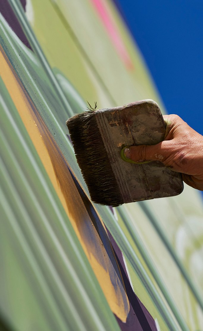 Una mano stende il colore sulla facciata con una grossa pennellessa